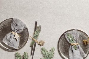 Christmas plate, rustic table setting, gray linen napkin on plate, knife, fork, decorated green fir tree on sacking tablecloth. New Year dinner or party idea, festive table setting photo
