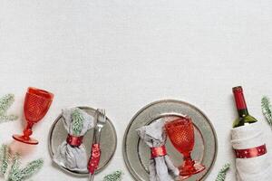 Tableware for Christmas or Xmas festive dinner, linen napkin on plate, knife, fork, red wine glass, bottle of wine on rustic tablecloth, New Year holiday cutlery, red decor, above view photo