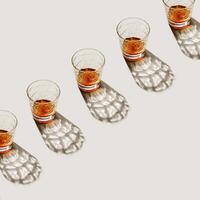 Crystal Whiskey Glasses at row with shadow and sunlight reflection on beige background, minimal neutral pattern, aesthetic top view summer still life, refraction at shine alcohol drinks, caustic photo