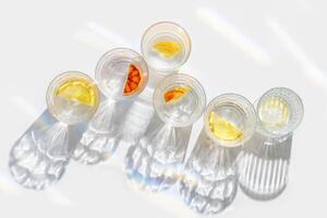 Citrus Infused Water in clear Glasses casting artistic light rainbow reflections and shadows at sunlight. Summer drink concept, minimal style pattern, flavored water with tasty slices of fruit photo