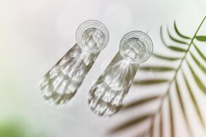 Water Glasses with palm leaf Shadows and sunlight Reflection on white background, colored photo minimal style, aesthetic top view summer still life, refraction throug crystal shine cups, caustic