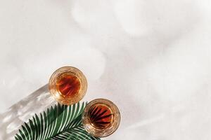 Whiskey Glasses with Shadow and sunlight Reflection on beige background, glass strong alcohol, palm leaf decor, aesthetic top view summer still life, refraction at crystal shine cups, caustics photo