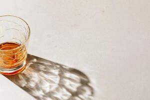 One crystal Whiskey Glass with shadow and sunlight reflection on beige background, neutral photo minimal style, aesthetic top view summer still life, refraction at shine alcohol drink, caustics