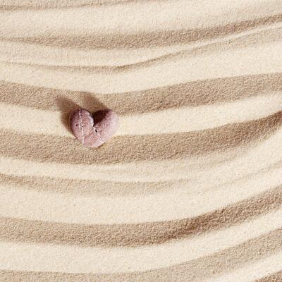 Sea stone form heart pale pink colored on natural fine sand background. Natural pebble, monochrome tones. Spa minimal background, concept for meditation and relax, love