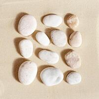 Pattern with white pebble sea stones on fine sand. Square composition from natural stone neutral beige color, monochrome tones photo