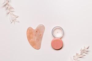 Guashe scrapes from rose quartz and cosmetic product bottle of cream Natural stone massager photo