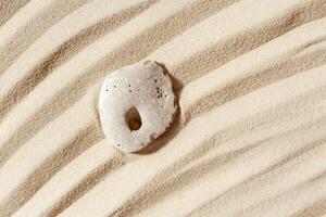 Minimal background with one stone with hole on fine sand with wave ripple. Natural happy stone light ivory color. Symbol of fun, fortunate, lucky. photo