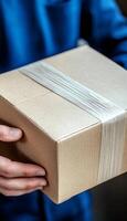 Delivery Person in Blue Uniform Holds Out a Securely Packaged Cardboard Box, Close Up photo