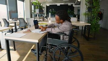 African American student in a wheelchair takes notes while studying at a desk with a laptop in a classroom video