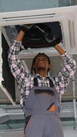 African American technician in overalls and helmet inspects a ceiling-mounted air conditioner unit inside a modern commercial office space video