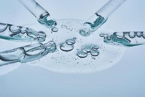 A large drop of hyaluronic serum for a blistered face and several pipettes on a blue background. photo