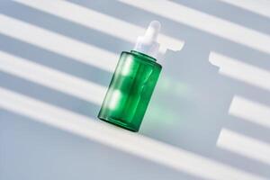 A green bottle of serum with Hydrolyzed sponge on a background with streaks of shadow. photo