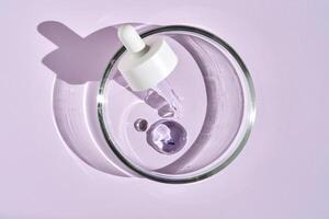 A pipette with a drop of serum in a petri dish on a purple background. photo
