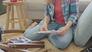 Woman sitting on floor and reading instruction manual while assembling wooden furniture video