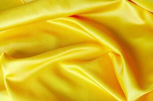 Vibrant yellow satin fabric draped in soft, smooth waves with a glossy finish. Suitable for design and wallpaper background. photo