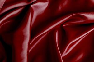 Top view of vibrant dark red fabric draped in soft, smooth waves with a glossy finish. Suitable for design and wallpaper background photo