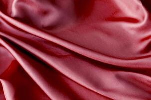 Vibrant dark red fabric draped in soft, smooth waves with a glossy finish. Suitable for design and wallpaper background photo