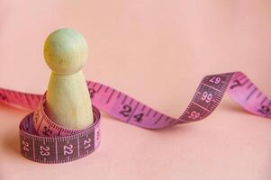 Pink measure tape wrapping a wooden doll with customizable space for text. Diet and copy space concept photo