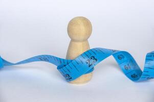 Blue measure tape wrapping a wooden doll with customizable space for text. Diet and copy space concept photo
