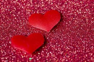 Side view of two tiny red hearts on sparkle red background with customizable space for text or wishes photo