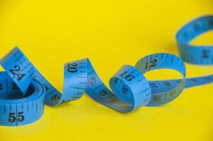 Blue tape measure on yellow background with customizable space for text. Dieting concept photo