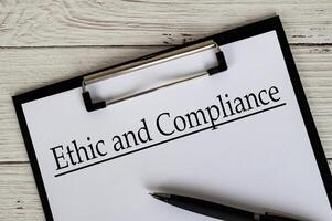 Clipboard with a document titled Ethic and Compliance text, placed on a white wooden surface. photo