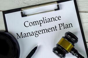 Top view of Compliance Management Plan text on white paper clipboard with gavel photo