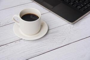Side view of white cup filled with black coffee and laptop with customizable space for text. Copy space concept photo