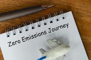 Top view of Zero Emission Journey text on white notepad with small airplane and pen background. Environmental awareness photo