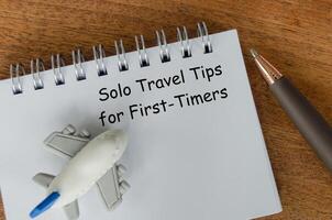 Solo Travel Tips for First Timers text on white notepad with toy airplane and pen photo