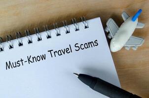 Must know travel scams text on white notepad with airplane and black pen background. photo