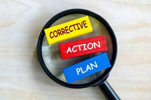 Corrective Action Plan text on colored wooden blocks with magnifying glass as background. Root cause analysis concept photo
