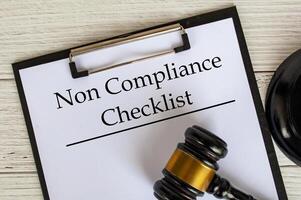 Top view of Non Compliance Checklist text on clipboard with gavel on top. Compliance concept photo