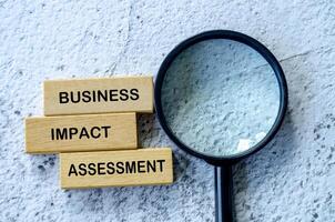 Top view of Business Impact Assessment text on wooden blocks with magnifying glass background photo