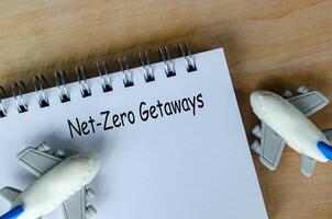 Top view of Net Zero Getaways text on white notepad with small airplanes background. Environmental awareness. photo