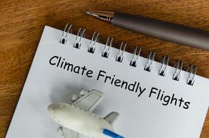 Top view of Climate Friendly Flight text on white notepad with small airplane and pen background. Environmental awareness photo