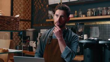 Puzzled Caucasian barista male waiter think manager man working in cafe entrepreneur using laptop employer seller arrange delivery on Internet staff guy browsing net computer restaurant small business video