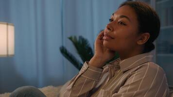 Portrait thoughtful dreaming African American woman rest on sofa in dark living room pensive dreamy girl homeowner think future plans dreams relaxing at night evening home look to side ponder thoughts video