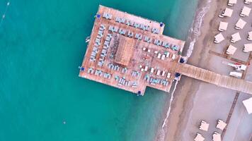 Drone view of beach umbrellas, turquoise sea, and pier at seaside resort video