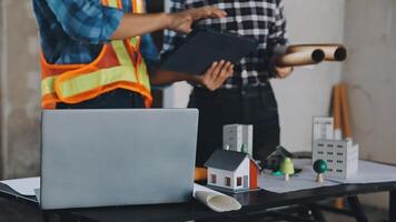 Two men in construction vests and hard hats are working on a laptop video