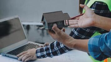 A man is holding a model of a house on a laptop video
