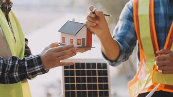 Two men holding a model of a house with a solar panel video