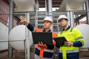 Two maintenance engineers inspect the condition of a large gas tank in a factory. photo