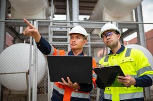 Two maintenance engineers inspect the condition of a large gas tank in a factory photo