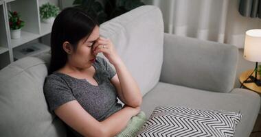 Handheld selective focus shot, Young woman sit on the sofa alone, lost in thought. Her brows were slightly furrowed and expression tense in the quiet atmosphere at home video