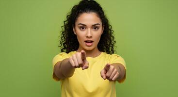 Woman Pointing Directly at Viewer in Yellow Top Against Green Background photo