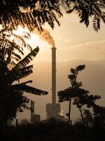 Smoke coming out of factory chimneys causes air pollution that contaminates the environment. Industrial waste is hazardous to public health. A chimney with evening and sunset view. photo