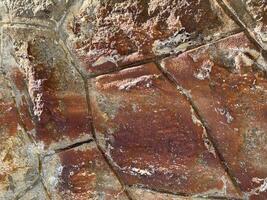 Close-up of a weathered red stone surface with cracks, rust stains, and textured erosion, evoking vintage architecture and raw urban atmosphere photo