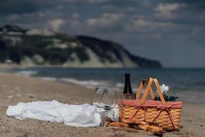 Elegant beach picnic with wine glasses and food by the sea under cloudy sky photo