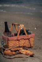 Romantic coastal picnic scene with basket wine and khachapuri on sandy beach. Beach Picnic with Wine and Pastries photo